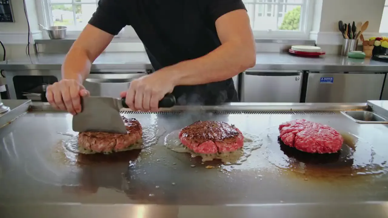 A cook pressing three smash patties down onto the flat-top griddle