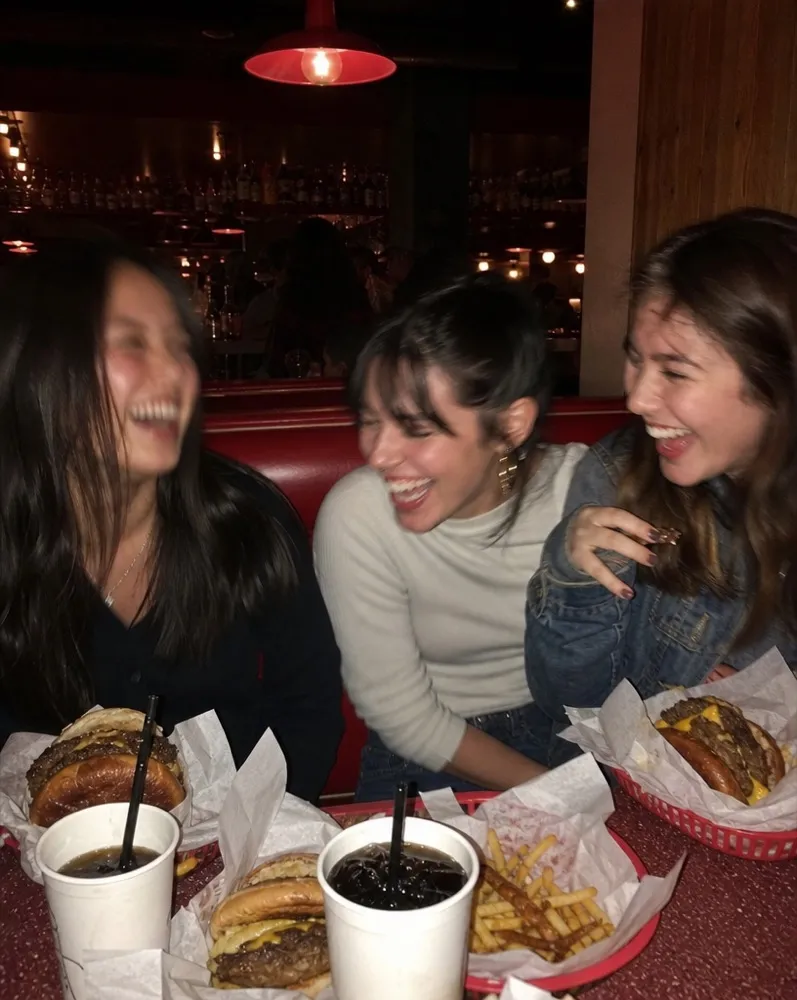 Three friends laughing over burgers in a red booth