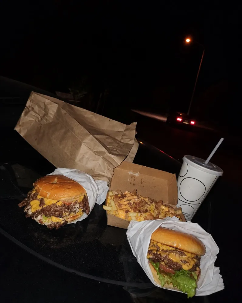 Burgers and loaded fries spread across a car hood at night