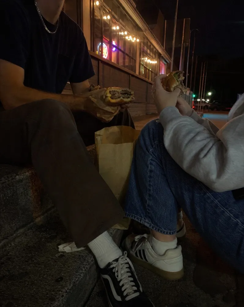 Two people eating burgers on the curb outside