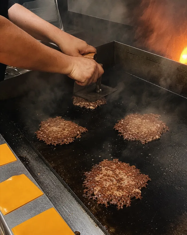 A cook pressing patties on the flat-top