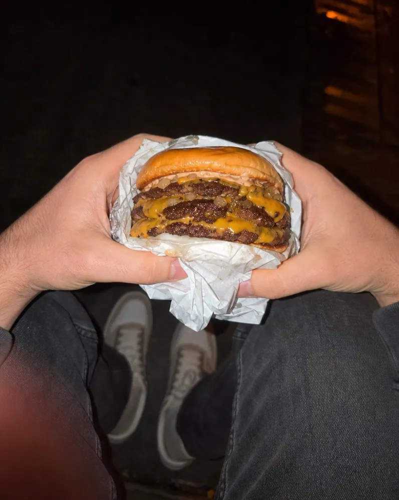 Hands unwrapping a double smash burger outside at night