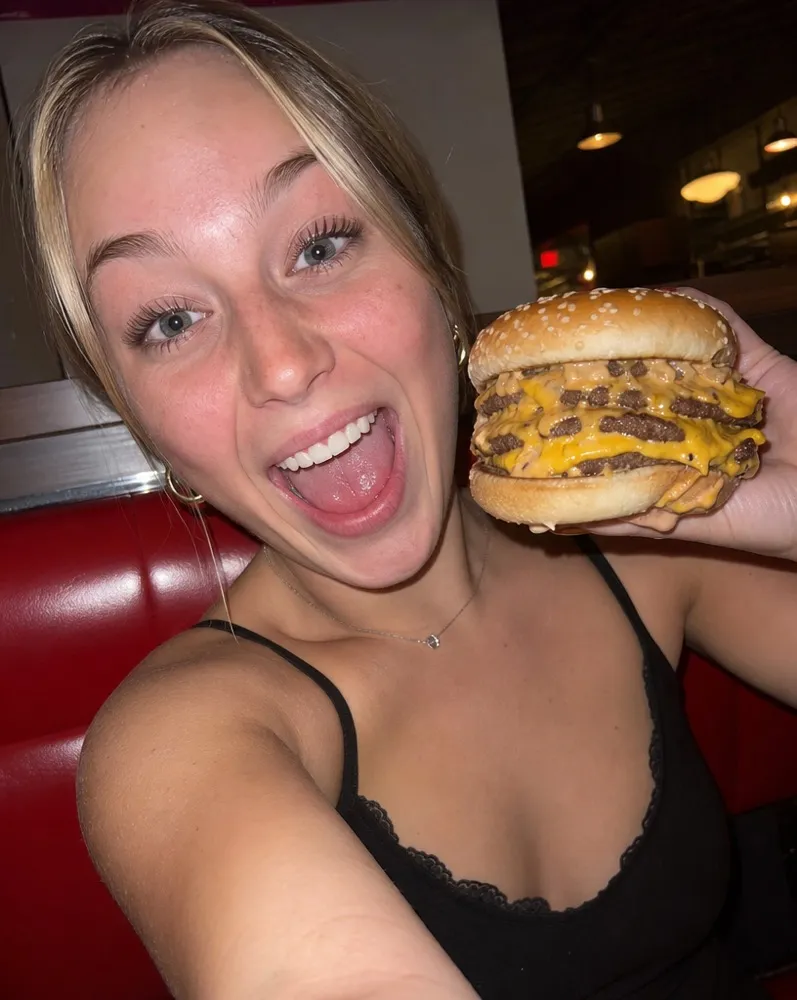 A customer holding a double smash burger up beside her face in a booth
