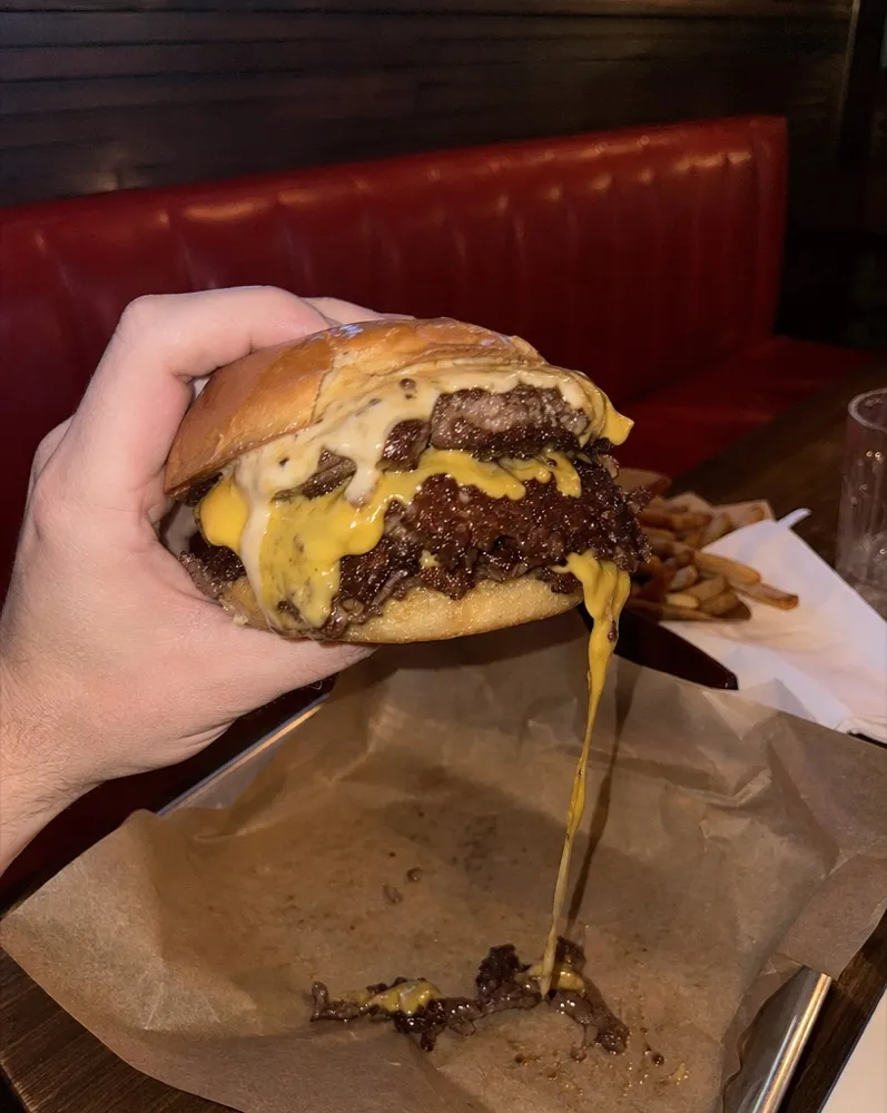 A double smash burger lifted off the tray, cheese pulling