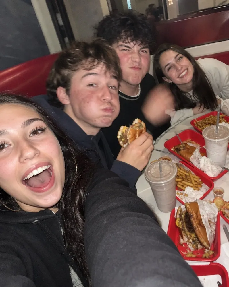 Four friends crowding into a selfie over trays of burgers and fries
