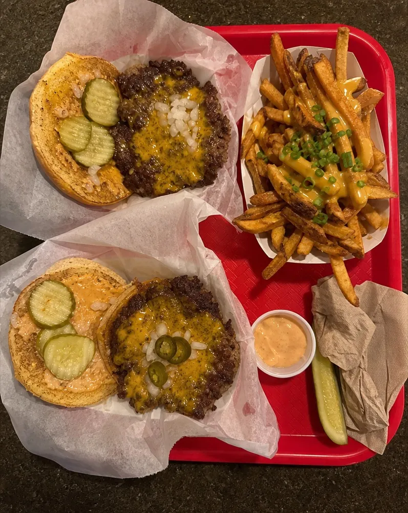 A red tray with two smash burgers and loaded fries